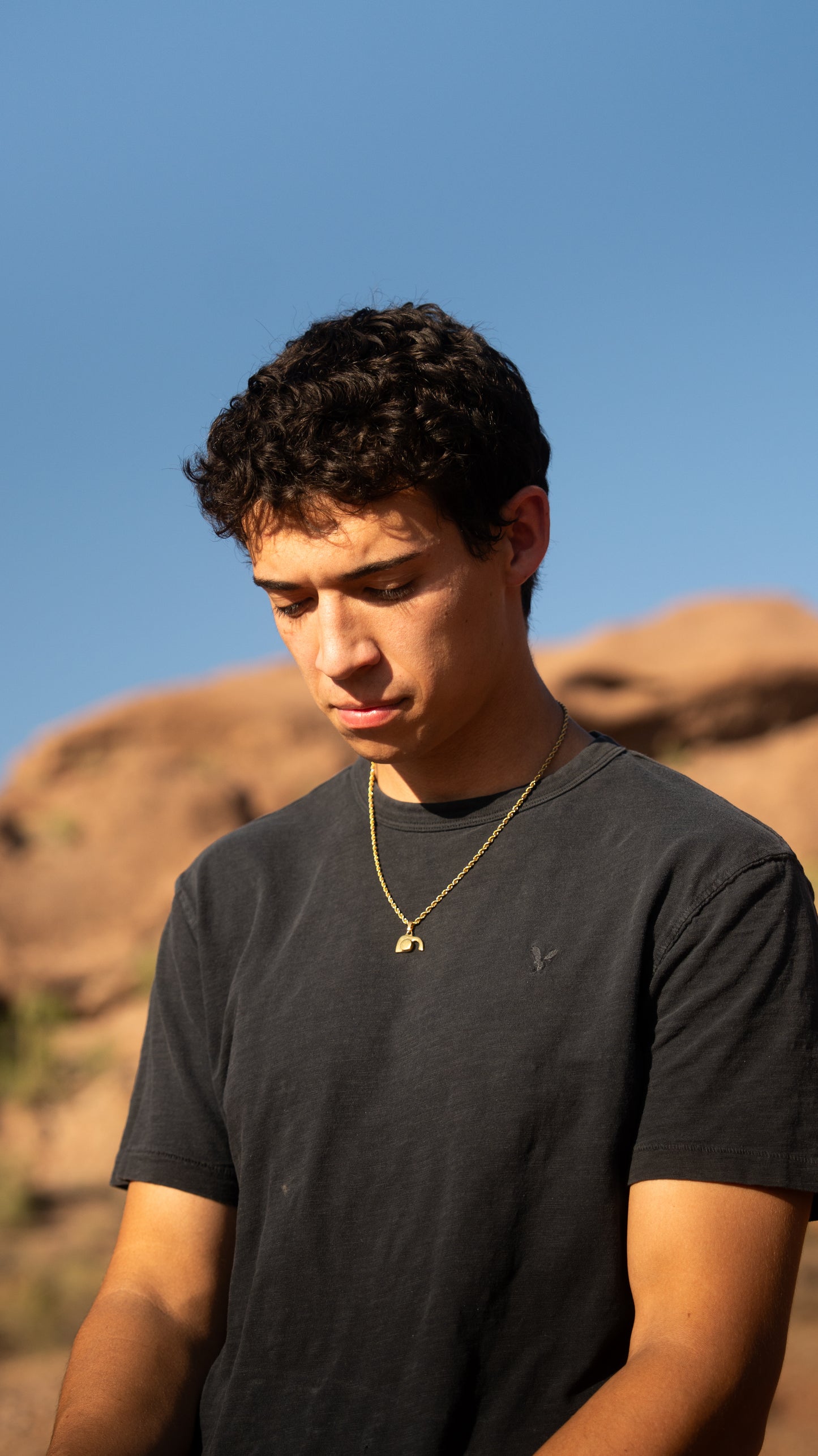 Man wearing a black t-shirt and gold empty tomb necklace against a desert landscape with clear blue sky.