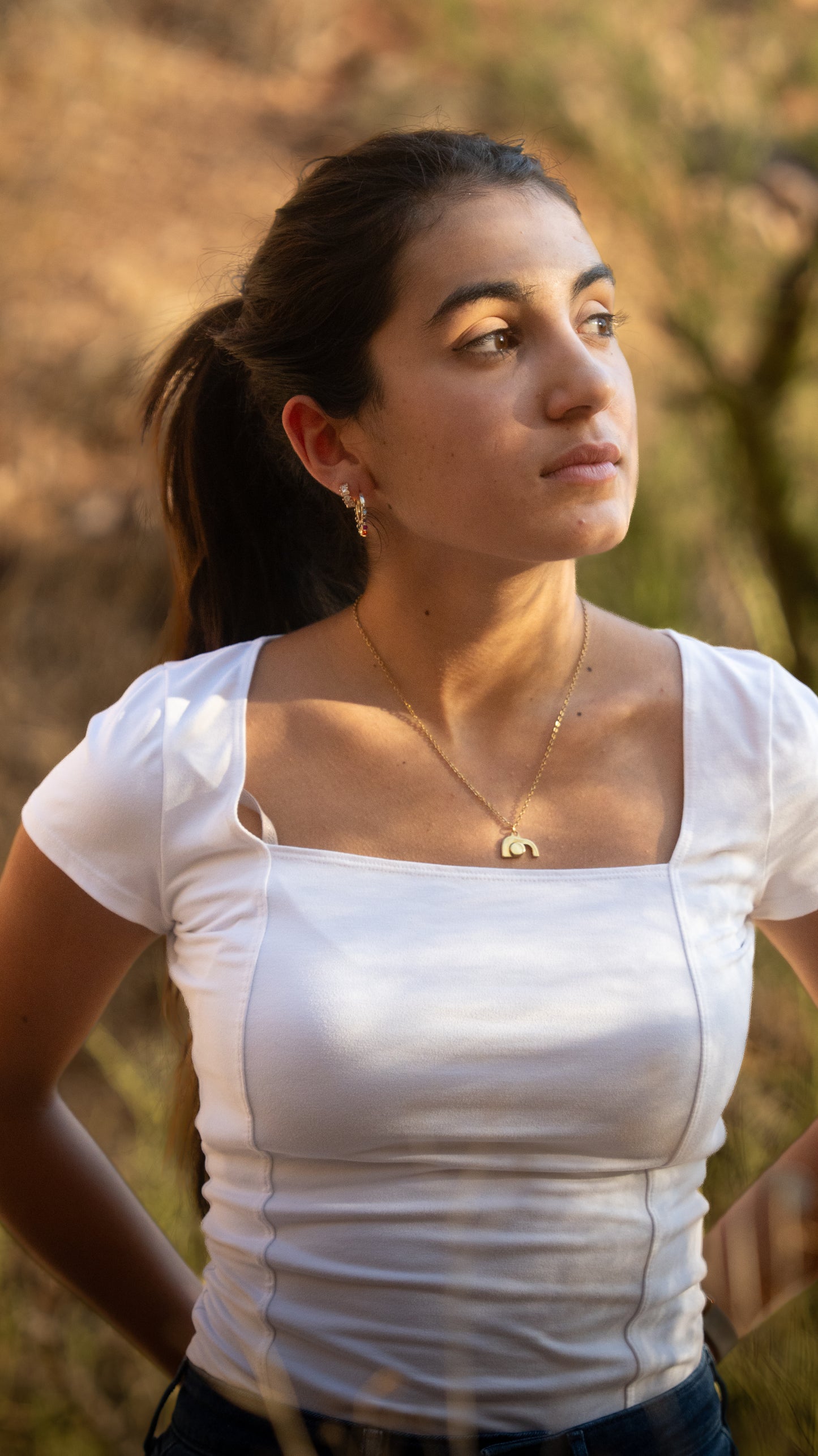 Woman wearing a white top and empty tomb necklace with a blurred natural background