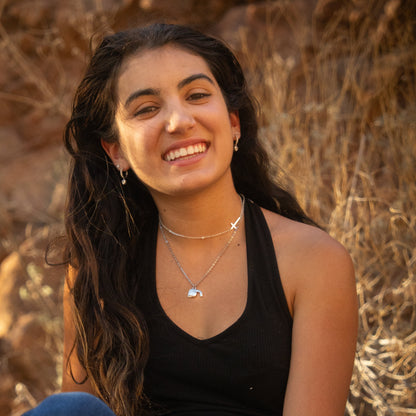 Woman wearing empty tomb necklace sitting outdoors with a warm, natural background
